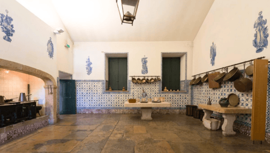 Historic kitchen with tiled walls, stone floor, and hanging pots.