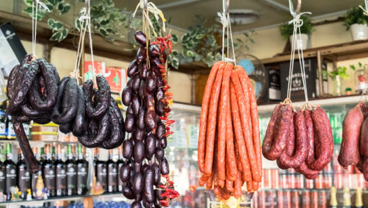 Various sausages hanging in a store with bottles on shelves.