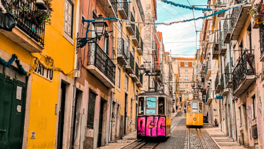 Two trams on a narrow street lined with colorful buildings and balconies.