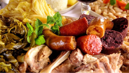 Assorted meats and sausages with leafy greens and cabbage on a plate.