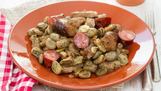 Plate of cooked broad beans and sliced sausage on an orange dish.