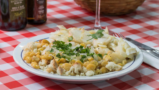 Plate of codfish with beans and herbs on checkered tablecloth.